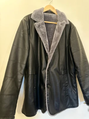 Svart skinnjacka med grå teddyfoder nytt skick  - Snygg svart skinnjacka med mjukt grått teddyfoder och krage. Jackan har knäppning med knappar framtill och två fickor med knappdetalj. Perfekt för kalla dagar och ger en cool vibe till din outfit.