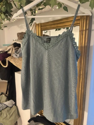 Grön spetsdetaljerad linnetopp från SHEIN - Säljer en grön linnetopp från SHEIN i storlek M. Toppen har tunna axelband, v-ringning och fina spetsdetaljer längs urringningen. Materialet är lätt och har ett diskret hålmönster som ger en romantisk vibe.