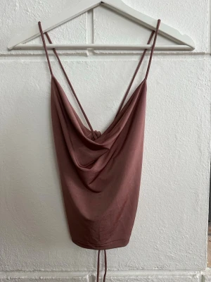 Brun linnetopp med snörning - Säljer en brun linnetopp. Toppen har öppen rygg med snörning som ger en snygg detalj. Prislappen sitter fortfarande kvar.