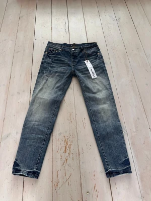Blå jeans från Purple Brand - Säljer ett par snygga blå jeans från Purple Brand med slitna detaljer och klassisk femficksdesign. Jeansen har en slim/normal passform, raka ben och är tillverkade i robust denim. Färgen är tvättad blå med ljusare partier för en cool, använd look.