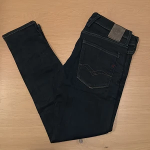 Replay Anbass jeans - Svarta Replay Anbass jeans med slim passform och klassisk femficksdesign. Snygga kontrastsömmar och detaljerad bakficka. Jeansen är tillverkade i stretchigt bomullsmaterial för extra komfort och har en modern, smal siluett som passar perfekt till sneakers.