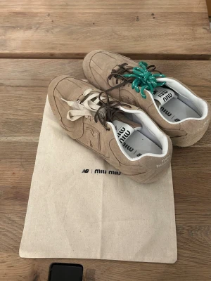 Beige sneakers 39  - Unika beige sneakers i mocka med en lyxig och trendig känsla. Skorna har olika färg på skosnörena, ett par är bruna, ett par vita och ett par gröna, vilket ger en subtil men lekfull detalj. Klassisk sportinspirerad sula och en diskret logga på sidan. Insidan är vit och helhetsintrycket är stilrent, modernt och genomarbetat.