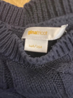 Mörkblå kabelstickad tröja Gina Tricot - Kabelstickad mörkblå tröja från Gina Tricot i storlek 146/152. Tröjan har korta ärmar, ribbade muddar och ett klassiskt kabelmönster. Perfekt för dig som gillar en enkel men ändå snygg look.