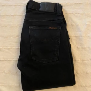 Svarta jeans från Nudie Jeans - Svarta jeans från Nudie Jeans med klassisk femficksdesign och snygga svarta sömmar på bakfickan. Jeansen har en stilren look med svart läderpatch i midjan och är tillverkade i mjukt denimtyg. Perfekta för dig som gillar en clean och tidlös stil. Tveka inte att höra av dig vid minsta fundering eller fråga. Dessa jeans är riktigt feta i passformen och är ett måste i garderoben. Pris ej hugget i sten!😁👊
