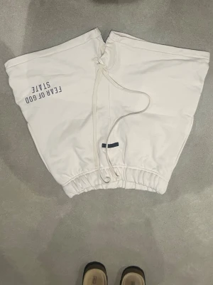 Fear of God Essentials vita shorts - Vita shorts från Fear of God Essentials med tryckt logga på vänster ben. De har elastisk midja med snörning och är tillverkade i mjuk bomull. Perfekta för chill dagar och har en loose fit som ger skön streetwear-vibe.