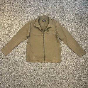  overshirt från Lyle & Scott - Säljer en oliv grön overshirt från Lyle & Scott med klassisk krage, bröstficka med logga och dragkedja framtill. Jackan är långärmad och har en stilren look som passar till många outfits. Inga defekter väldigt fint skick. 