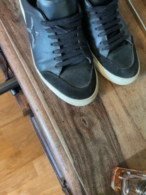 Svarta Arigato sneakers med broderad fågel - Säljer ett par svarta sneakers från Arigato med broderad fågel på sidan. Skorna har svarta snören, vit sula och detaljer i både skinn och mocka. Perfekta för dig som vill ha en clean men ändå unik look.