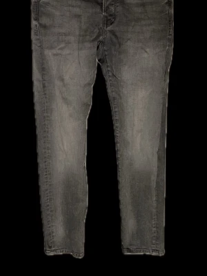 Grå slim jeans från Jack & Jones - Säljer ett par gråa slim fit jeans från Jack & Jones, modell Glenn. Jeansen har klassisk femficksdesign, svarta knappar och en snygg tvättad look. Materialet är mjukt jeans-tyg som sitter tajt men ändå bekvämt. Perfekta för dig som gillar en smalare passform.