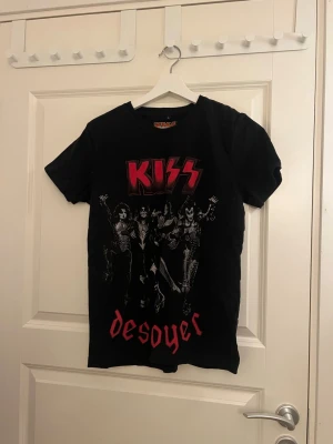 KISS Destroyer svart t-shirt - Svart t-shirt med KISS Destroyer-tryck i rött och vitt framtill. Klassisk rund hals och korta ärmar. Perfekt för dig som gillar rock och vill sticka ut med en ikonisk bandtröja.