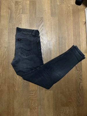 Svarta skinny jeans från Lee Malone - Säljer ett par svarta skinny jeans från Lee med diskret tvättad look. Jeansen har klassisk femficksdesign, normal midja och smala ben hela vägen ner. Materialet är mjukt och stretchigt för extra komfort. Perfekta till sneakers eller boots.