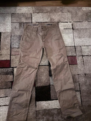 Beige chinos från Morris, storlek 30/32 - Säljer ett par klassiska beige chinos från Morris i storlek 30/32. Byxorna är tillverkade i mjuk bomull med lite stretch för extra komfort. De har normal passform, raka ben och snygga detaljer vid midjan. Perfekta till en clean och stilren look. Om ni undrar något så kan ni kontakta mig!