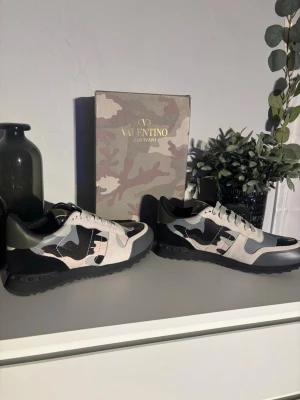Valentino Garavani Rockrunner sneakers - Säljer ett par Valentino Garavani Rockrunner sneakers i svart, grått och beige med camouflage-mönster. Skorna har snörning, platt sula med nitar och detaljer i mocka, skinn och textil. Ikonisk logga på plös och innersula. Riktigt snygga och unika sneakers!