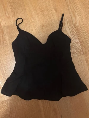 Svart linne från Zara - RESERVERAD. Säljer en svart linne topp från Zara med justerbara smala axelband, en dragkedja vid ena sidan och lätt utsvängd nederkant. Toppen har en figurnära passform och smockad rygg för extra komfort. Det finns ett litet hål nedanför dragkedjan men det är inget man tänker på. 