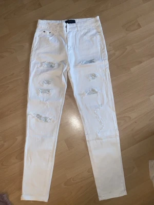 Amiri jeans - Säljer ett par vita skinny jeans från Amiri med flera slitningar och hål framtill. Byxorna har klassisk femficksdesign och är tillverkade i ett stretchigt bomullsmaterial. Perfekta för dig som gillar en edgy och trendig stil. Knappt använda dem va för stora. Pris kan diskuteras och kan även byta 