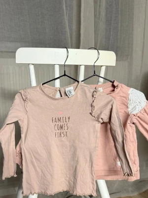 Två rosa långärmade toppar barn - Säljer två söta långärmade toppar i ljusrosa toner. Ena toppen från H&M har volangdetaljer på axlarna och texten 'Family Comes First' framtill. Den andra från Newbie har broderade vita axelpartier och ribbade muddar. 
