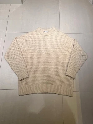 Beige stickad tröja från Zara - Säljer en beige stickad tröja från Zara i storlek M. Tröjan har en chunky struktur med grov ribb vid ärmslut och nederkant. Perfekt för kyliga dagar och enkel att styla med allt. Rund hals och långärmad modell.