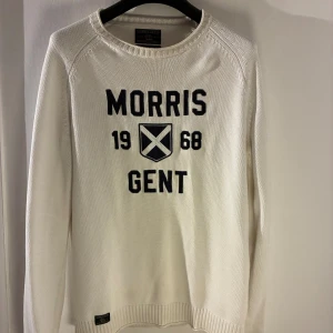 Morris Gents – Stickad tröja Medium - Säljer en vit stickad tröja från Morris Gents i storlek Medium. Tröjan har broderad logga och text på framsidan samt ribbade muddar vid ärmar och nederkant. Materialet är mjukt och sitter bra utan att vara tight. Den är sparsamt använd och i bra skick utan några skador eller fläckar. Nypris ligger runt 1 299–1 499 kr.