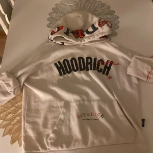 Vit hoodie från Hoodrich med tryck - Säljer en vit hoodie från Hoodrich i storlek S. Tröjan har stor svart logotyp på bröstet, coolt tryck på huvan och text på ryggen. Klassisk känguruficka framtill och långa ärmar. Materialet är mjuk bomull, perfekt för chill dagar. Väldigt Snygg och bra tröja för att hålla dig varm i Vintern som kommer! köpt för 2200 Säljer för 1500 Väldigt Bra Pris. Skulle rekommendera att köpa denna tröjan!