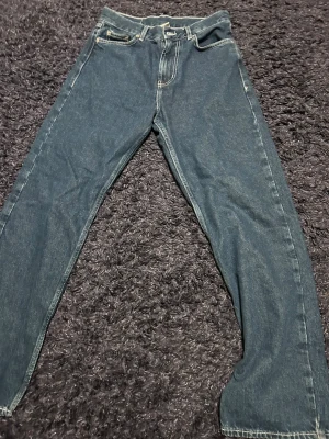 Blå jeans District Fortysix X-Small - Snygga blå jeans från District Fortysix i storlek X-Small. Klassisk femficksmodell med gul broderad logga på bakfickan och coolt märke vid midjan. Jeansen har raka ben och kontrastsömmar, tillverkade i Turkiet av slitstarkt denimtyg.