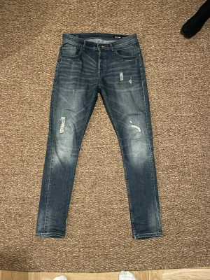 Blå jeans från Only & Sons - Snygga blå jeans från Only & Sons med skinny passform och slitna detaljer på framsidan. Jeansen har klassisk femficksdesign, normal midja och är tillverkade i stretchigt denim för skön komfort. Perfekt för dig som gillar en unik design.