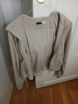 Beige hoodie från Gina Tricot - Säljer en beige hoodie från Gina Tricot i storlek S. Tröjan har dragkedja framtill, huva och långa ärmar. Materialet är mjukt och känns som fleece, perfekt för chill dagar. Snygg och enkel design med normal passform.