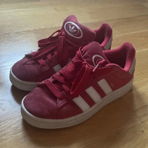 Röda Adidas sneakers strl 38 - Säljer ett par snygga röda Adidas sneakers med klassiska vita ränder på sidorna och Ortholite-innersula för extra komfort. Skorna har rund tå, snörning och en platt vit sula. Sparsamt använda och bara använda ett fåtal gånger, säljs då dom är försmå.