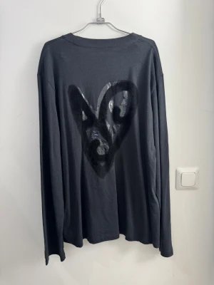 Svart långärmad tröja Acne Studios med hjärta i velour storlek M - Svart långärmad tröja från Acne Studios med ett coolt hjärtmotiv i silver och svart på bröstet och ryggen. Tröjan har rund hals och är gjord i mjuk bomull, perfekt för dig som gillar stilrena plagg med en twist.