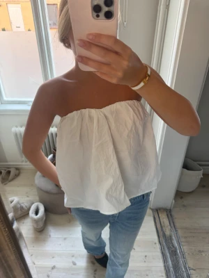 Vit bandeau tubtopp i bomull - Säljer en vit bandeau tubtopp med luftig och lös passform. Toppen är axelbandslös och har en lätt rynkad effekt upptill. Materialet är bomull och toppen är perfekt för varma dagar. Enkel och stilren design som är lätt att matcha med jeans eller kjol. Lapp kvar 🩷🩷🩷🩷