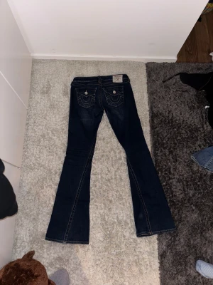True Religion mörkblå bootcut jeans - Mörkblå jeans från True Religion. Har bakfickor med knapp och märkets logga. Strl 25 i midjan och är lagom långa på mig som är 168, men skulle absolut funka på någon längre.