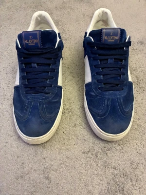 Valentino flycrew skor - Snygga sneakers från Valentino Garavani i mörkblå mocka med vita detaljer och platt sula. Skorna har rund tå, snörning och en klassisk siluett. Märkeslogga på plösen och insidan är vit. Perfekt för dig som gillar exklusiva streetwear-vibes. Färgen heter royal blue. Öppen för prisförslag samt byten. Tveka inte på att höra av er vid frågor eller funderingar!