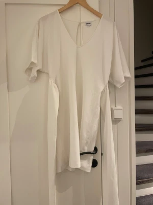 Vit omlottklänning från Bubbleroom - Snygg vit kortklänning från Bubbleroom med omlottdetalj i midjan och v-ringad hals. Klänningen har korta ärmar och ett stilrent, minimalistiskt uttryck. Perfekt för dig som gillar enkel och fräsch stil. Materialet känns mjukt och lätt mot huden.