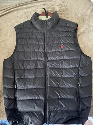Svart dunväst från Polo Ralph Lauren - Svart dunväst från Polo Ralph Lauren med hög krage, köptes för någon månad sen 2300kr. Den är i storlek L men passar M ifall man gillar den lite lösare, och passar L perfekt. Snygg till vår, höst men även lager på lager till en kall vinter dag. Pris kan diskuteras vid snabb affär! 