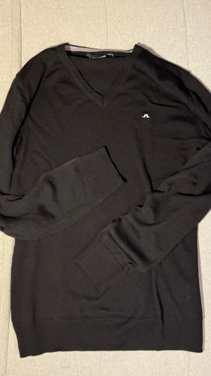 Helt ny! Svart v-ringad tröja J.Lindeberg - Svart v-ringad tröja från J.Lindeberg med diskret logga på bröstet. Materialet är mjuk bomull som känns skönt mot huden. Perfekt för dig som gillar stilrena och enkla plagg. Aldrig använd! Helt ny! Nypris 1300kr