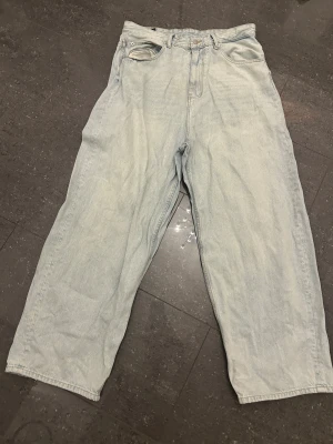 Ljusblå wide jeans från Pull&Bear - Säljer ett par ljusblå jeans från Pull&Bear med relaxed wide fit och hög midja. Klassisk femficksmodell med dragkedjegylf och snyggt läderpatch bak. Perfekta för en chill och trendig look.