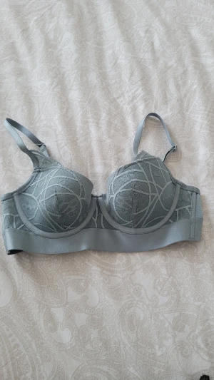 Turkos spets-bh från Hunkemöller 70B - Snygg turkos bh från Hunkemöller i storlek 70B med spetsdetaljer och mönstrad framsida. Bh:n har justerbara axelband och slät baksida för extra komfort. Perfekt för dig som gillar stilrena underkläder med en twist.
