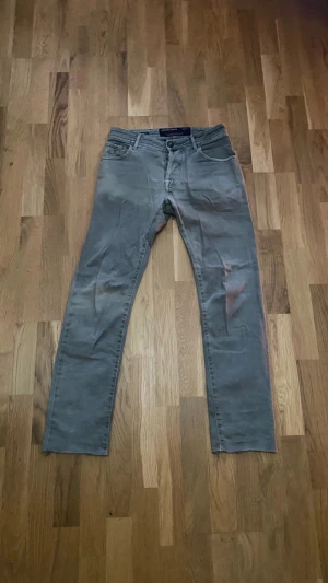 Grågröna jeans från Jacob Cohen - Snygga grå jeans från Jacob Cohen med klassisk femficksdesign och raka ben. Byxorna har en mörkgrön patch bak i midjan och ett broderat J på fickan. Materialet är mjukt och stretchigt, vilket gör dem riktigt sköna att bära. Perfekt för dig som gillar stilrena och tidlösa jeans. Storlek 32, sitter som en blandning av slim och straight.  Tveka inte på att skriva vid frågor eller funderingar!