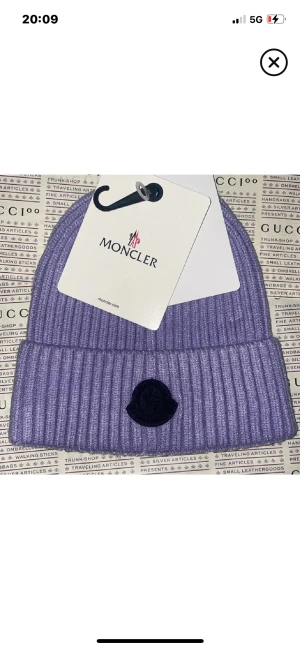 Lila ribbad mössa från Moncler - Snygg lila mössa från Moncler med ribbad design och uppvikt kant. Mössan har Moncler-logga framtill i mörk ton och är tillverkad i mjukt stickat material som håller dig varm och ger en cool vibe.