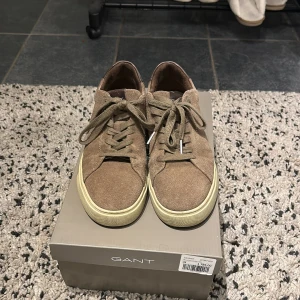 Beige mockasneakers från Gant, strl 42 - Snygga sneakers från Gant i beige mocka med klassisk snörning och vit platt sula. Skorna har rund tå och diskret Gant-logga baktill. Perfekta för dig som gillar stilrena och tidlösa sneakers med premiumkänsla.
