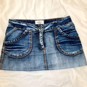 Jeanskjol - Snygg blå jeanskjol från L.O.G.G. med slitna detaljer och kontrastsömmar. Kjolen har stora rundade framfickor och bakfickor med lock och knapp. Klassisk knapp- och dragkedjestängning framtill. Perfekt för en cool look.