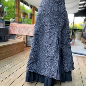 Svart långkjol med mönster från Onetwo 40 - Elegant kjol i svart /grå med ett subtilt, mönstrat tryck. Kjolen har en intressant design med rynkade detaljer framtill och en underkjol som ger en fin silhuett och extra volym. Perfekt för både vardag och fest. Längd: 79 cm ﻿Midja: 80 cm ﻿52% polyester ﻿48% polyamid  Inga bilder när den sitter på mig! Katter finns i hemmet!