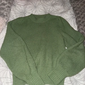 Grön stickad tröja från Monki - Säljer en grön stickad tröja från Monki i storlek XS. Tröjan har ribbad struktur, rund hals och långa ärmar med lätt puff vid axlarna. Perfekt för dig som gillar mjuka och mysiga plagg med lite volym i ärmarna.