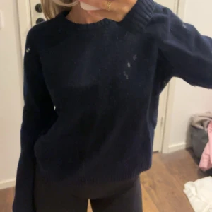 Mörkblå stickad tröja med rund hals - Snygg mörkblå stickad tröja med rund hals och långa ärmar. Tröjan har en klassisk, enkel design med ribbade muddar vid hals, ärmslut och nederkant. Perfekt för dig som gillar en chill och stilren look. Material: Ull