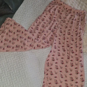Byxor - Säljer ett par supermysiga rosa byxor från 157 med blommigt mönster. De har en loose passform och elastisk midja för extra komfort. Perfekta för chill dagar och har en skön, mjuk känsla. Inget synligt slitage eller defekter-lite nopprigt bara