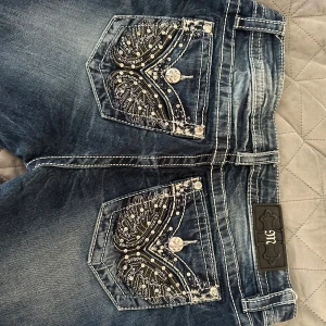 Lågmidjade Miss Me jeans  - Snygga blå jeans från Miss Me med bootcut passform och coola broderade bakfickor med paljetter och detaljerade knappar. Jeansen har kontrastsömmar och är lågmidjade. Perfekt för dig som gillar statement-plagg och unik stil. Nyskick!! Pris går att diskutera!💓storlek: 29 och midjemått:37