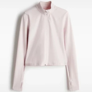 Ljusrosa croppad zip-jacka - Säljer en ljusrosa croppad jacka med dragkedja framtill och lång ärm. Jackan har en clean look med hög krage och är tillverkad i ett mjukt, stretchigt material. Perfekt för en sportig och trendig stil.