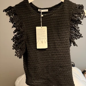 Topp - Snygg svart topp från Zara i ett stickat material med dekorativa spetsdetaljer på axlarna. Perfekt för både vardag och fest! Toppen är i nytt skick med etikett kvar 🌸