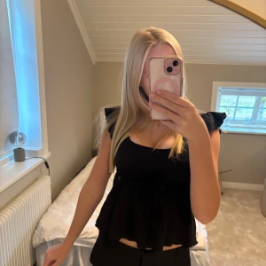Svart blus med volang och knyt - Säljer en så fin blus/topp från nelly då den inte används längre. Den knyts under bysten och har volang på axlarna och ner till🤍