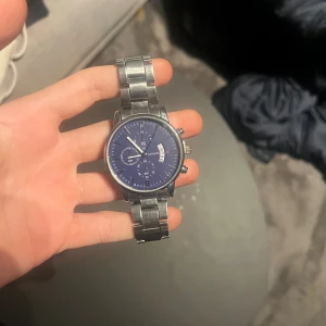 Blå kronografklocka från Geneva - Snygg kronografklocka från Geneva med blå urtavla och silverfärgat armband i metall. Klockan har flera små visare, datumvisning och en rund boett. Perfekt accessoar för dig som gillar stilrena detaljer och klassisk design.