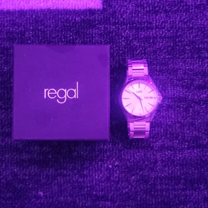 Regal GHW silverfärgad klocka - Stilren klocka från Regal med GHW på urtavlan. Klockan har rund form, silverfärgad länkarmband i rostfritt stål och vit urtavla med dag- och datumvisning. Levereras med originalask och extra länkar. Perfekt accessoar för dig som gillar klassisk design.