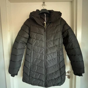 Svart pufferjacka från Slazenger - Svart pufferjacka från Slazenger i storlek M. Jackan har huva, långa ärmar och dragkedja framtill. Quiltad design med horisontella sömmar och en clean look som funkar till många stilar. Perfekt för kalla dagar när du vill vara både varm och snygg.